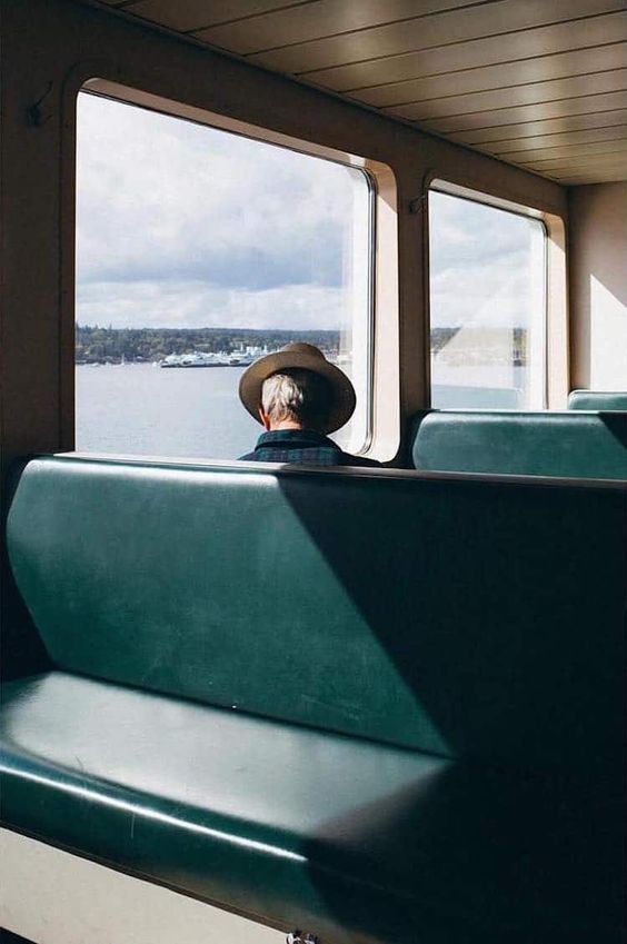 a man wearing a cowboy hat sitting on a bus looking out the window at the water