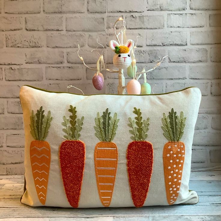 a white pillow with carrots on it sitting in front of a brick wall and an easter decoration