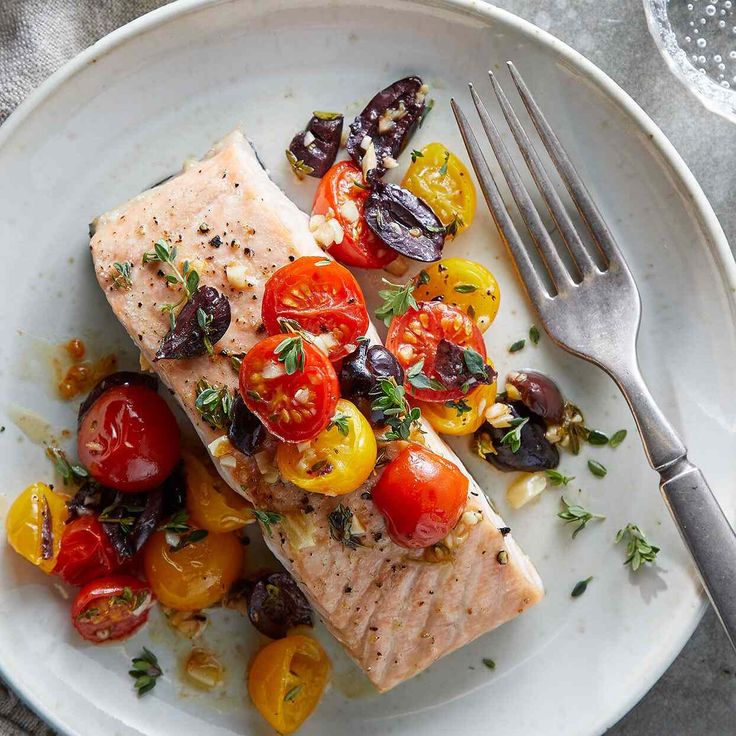 a white plate topped with fish, tomatoes and olives on top of a table