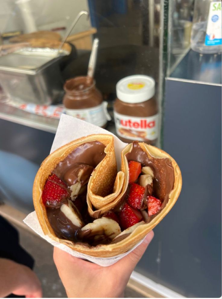 a person holding up a pastry with chocolate and strawberries in it's wrapper