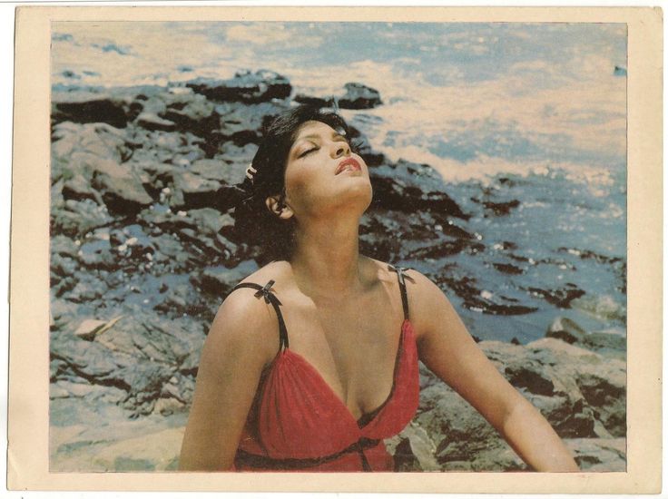 a woman in a red swimsuit sitting on rocks by the ocean with her eyes closed