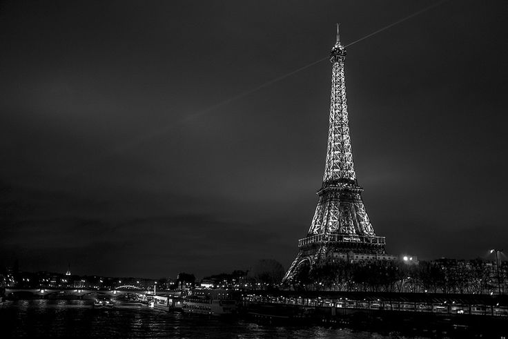 the eiffel tower lit up at night in black and white, as seen from across the river