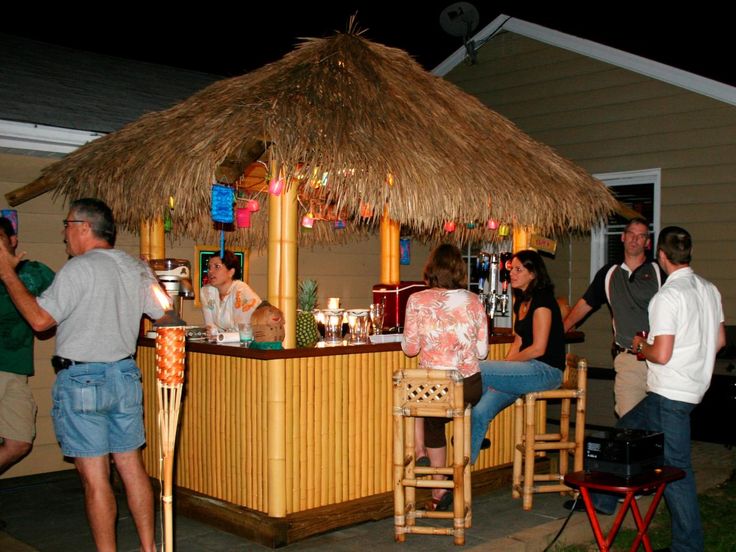 a group of people standing around a bar with tiki hut on it's roof