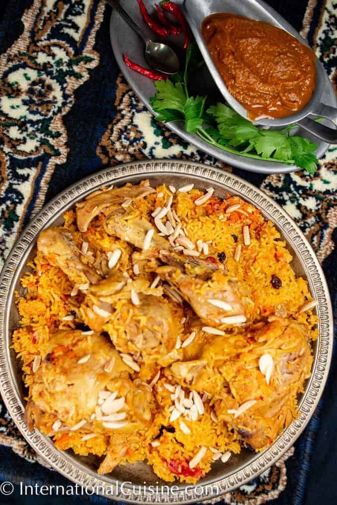 a silver plate topped with chicken and rice next to a bowl of sauce on a table