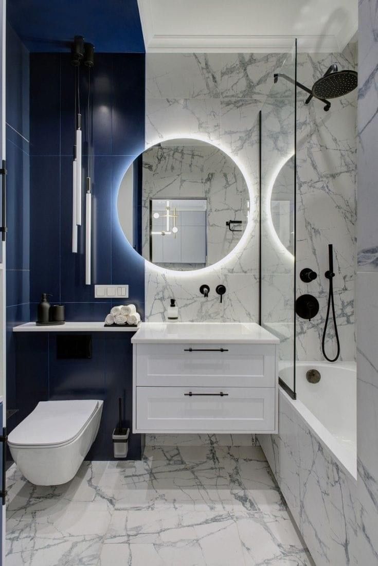 a white and blue bathroom with round mirrors on the wall above the sink, toilet and bathtub