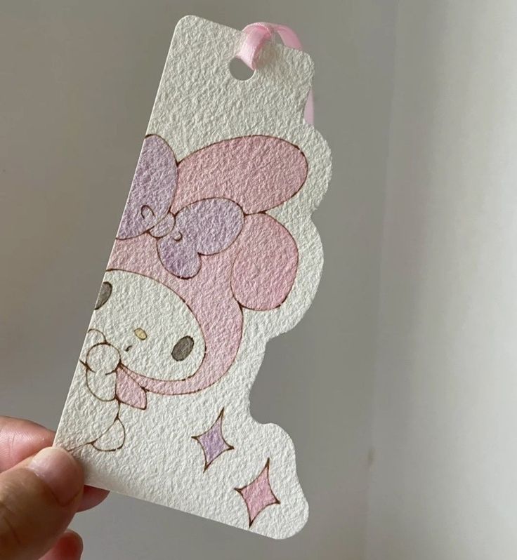 a hand holding up a pink and white tag with a cartoon bear on it's face