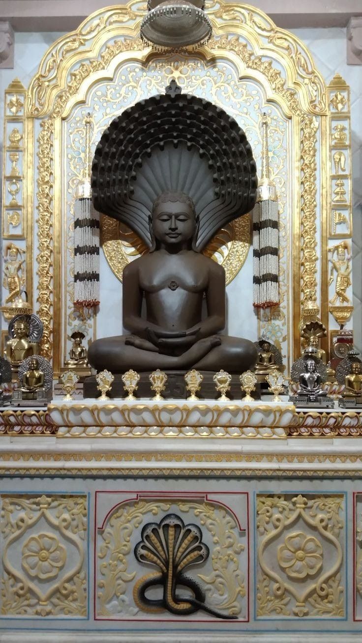 the buddha statue is sitting in front of an ornate gold and white wall with carvings on it