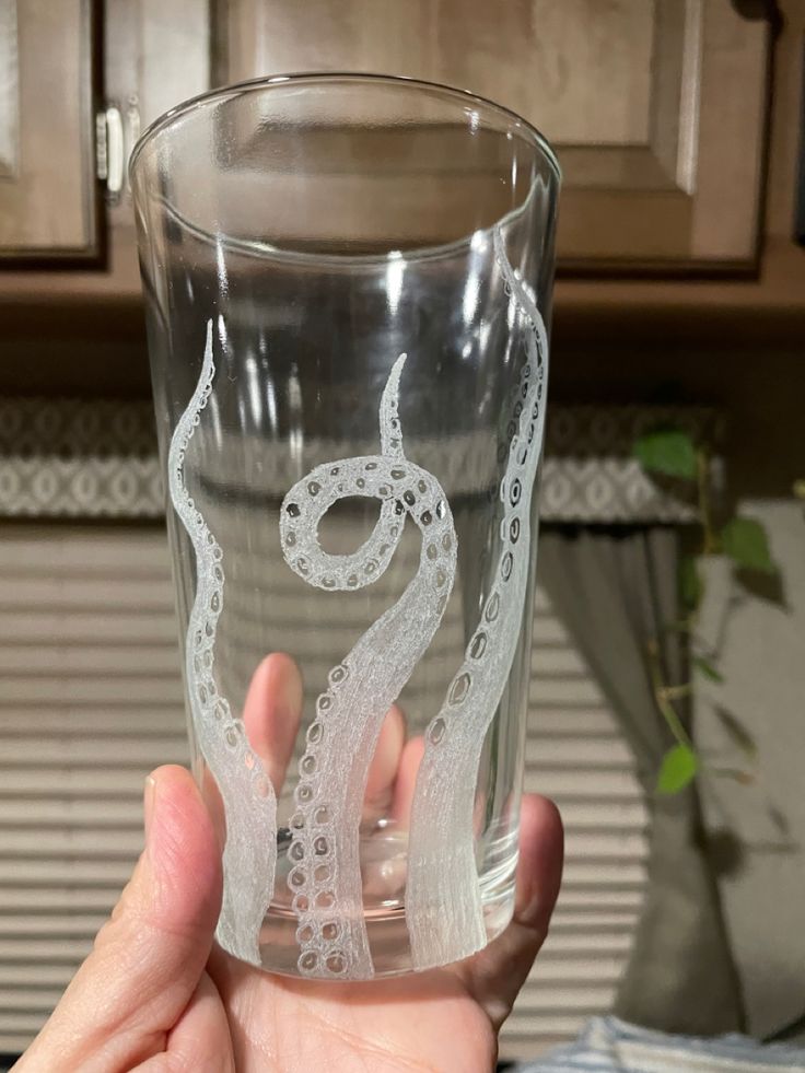 a person holding up a glass with an octopus drawn on the side and inside it