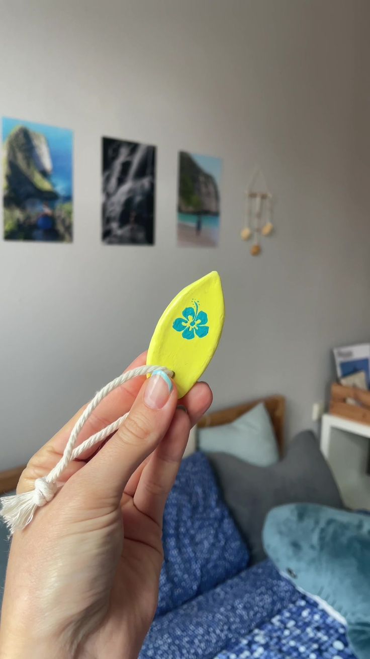 a hand holding a yellow frisbee in front of a bed with pictures on the wall