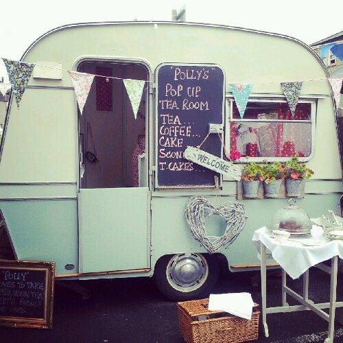 an old camper is parked in a parking lot with flowers and bunting on it