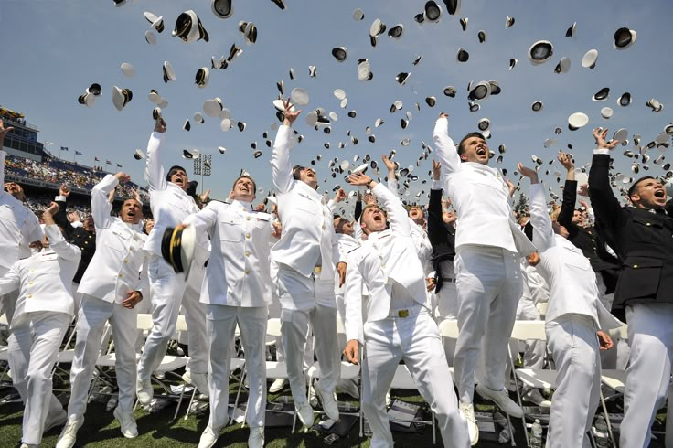 a group of people in white suits throwing caps into the air