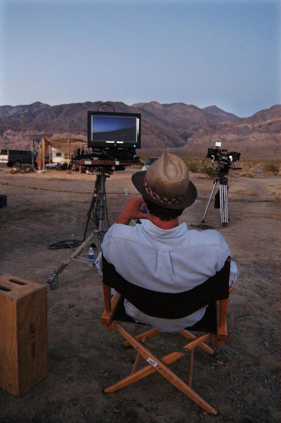 a man sitting in a chair with a television set on top of him and mountains behind him