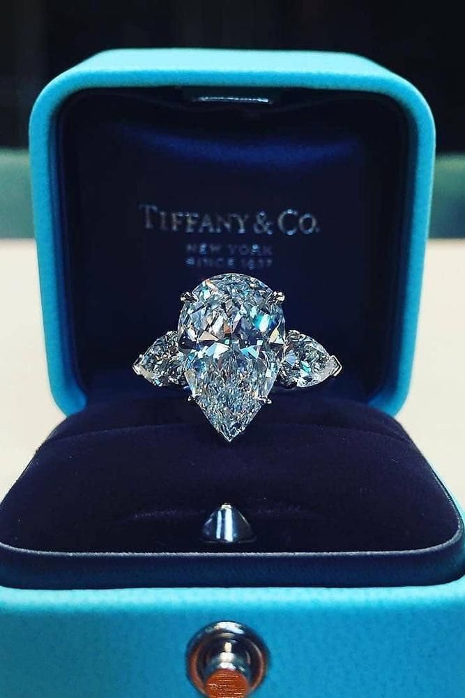 an engagement ring with three pear shaped diamonds in a blue velvet box on top of a table