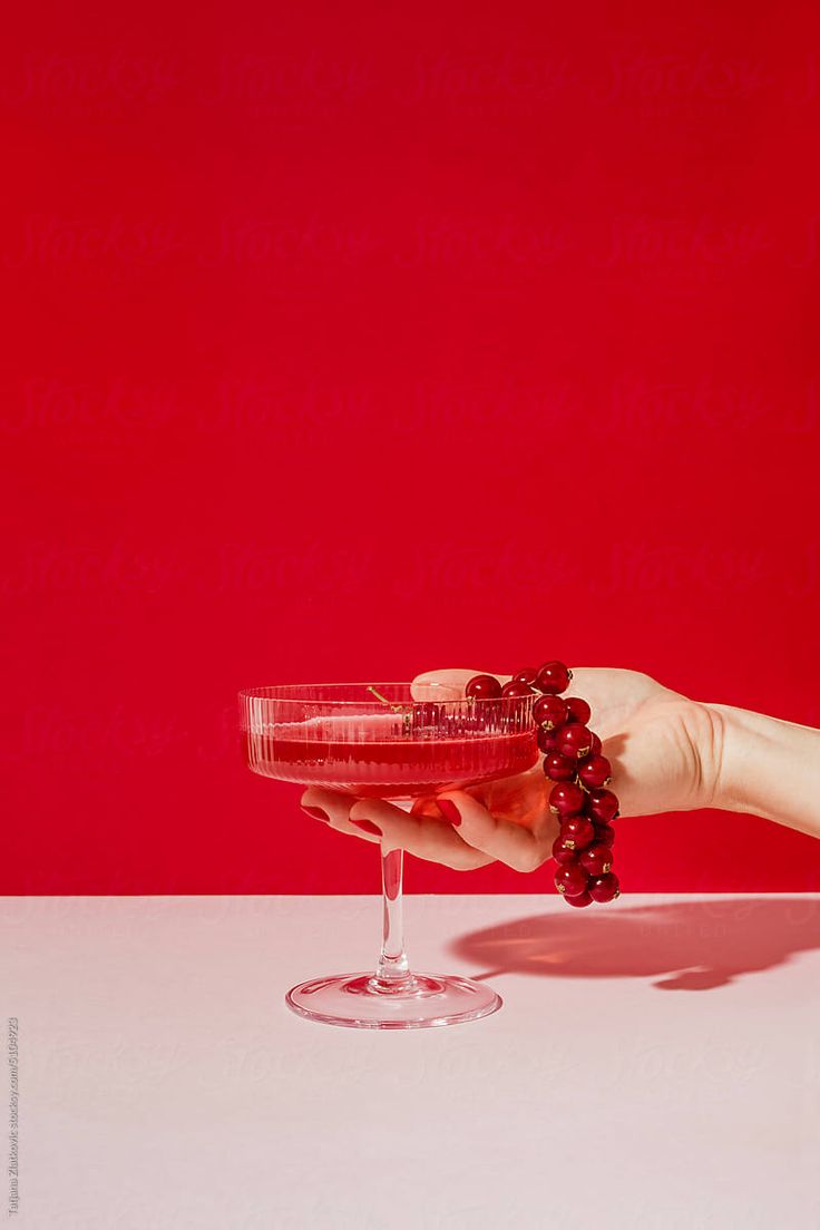 a hand holding a wine glass with grapes in it on a white table next to a red wall