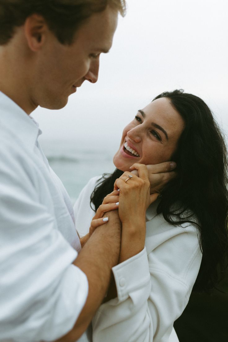 a man and woman standing next to each other near the ocean smiling at each other