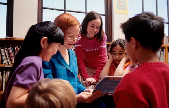 a group of young children standing around each other in front of a book shelf with books on it