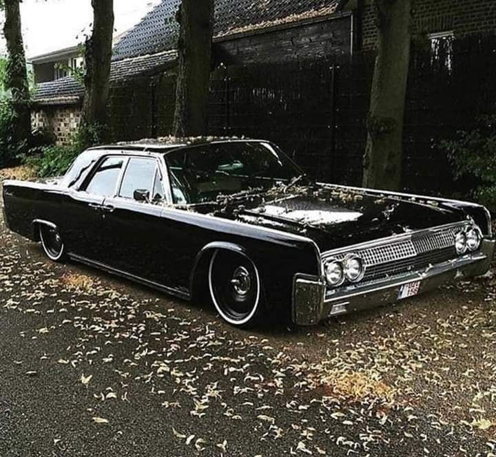 an old black car parked on the side of the road in front of some trees