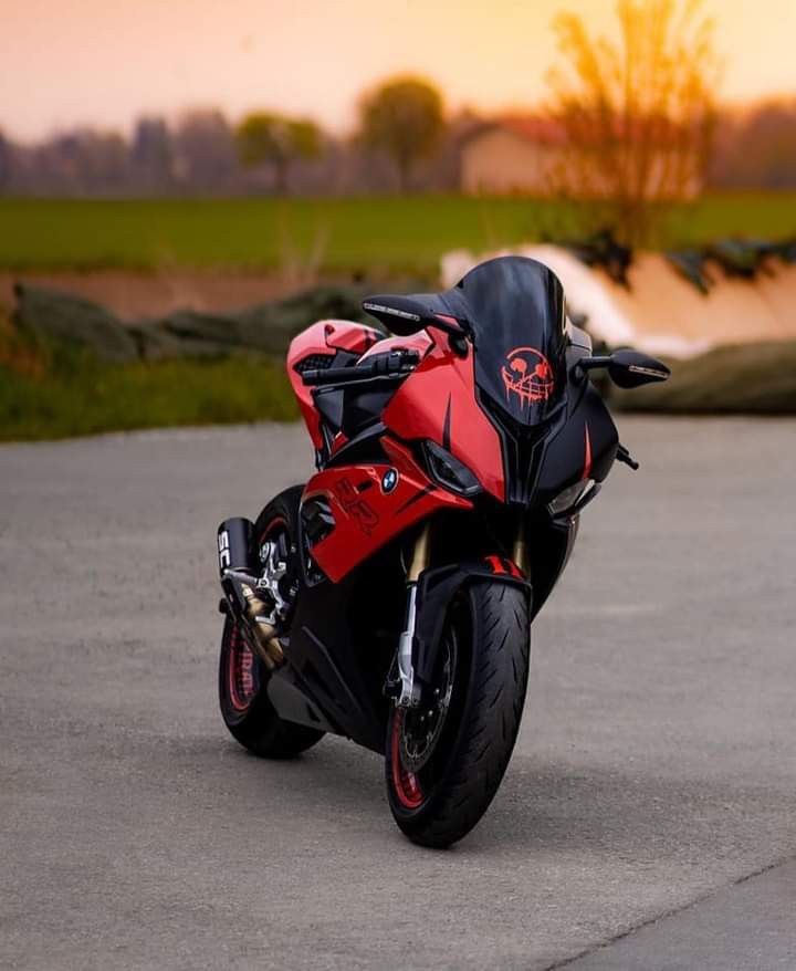 a red and black motorcycle parked on top of a cement road next to a field