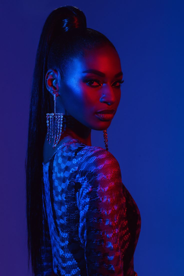 a woman with long black hair and earrings on her head, standing in front of a blue background