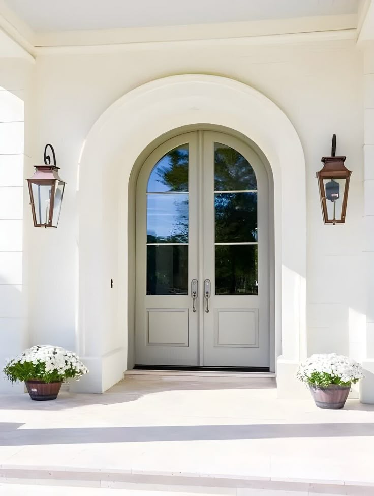 two potted flowers sit on the front steps of a white house with double doors