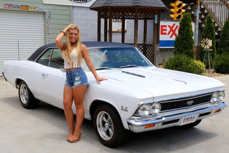 a woman leaning on the hood of a white muscle car in front of a garage