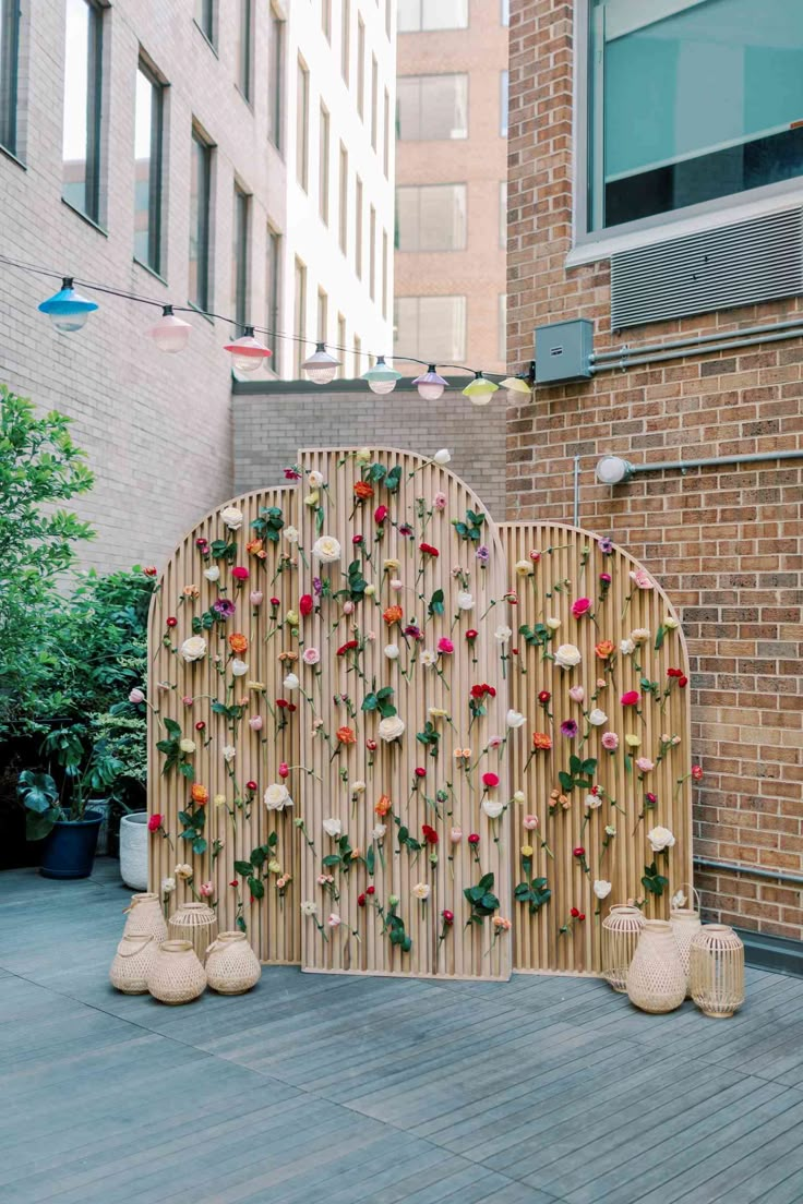 a bamboo fence with flowers on it in front of a brick wall and planters