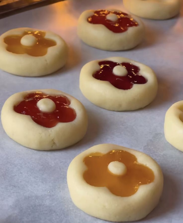 small cookies with jelly and cream fillings sitting on a baking sheet, ready to go into the oven