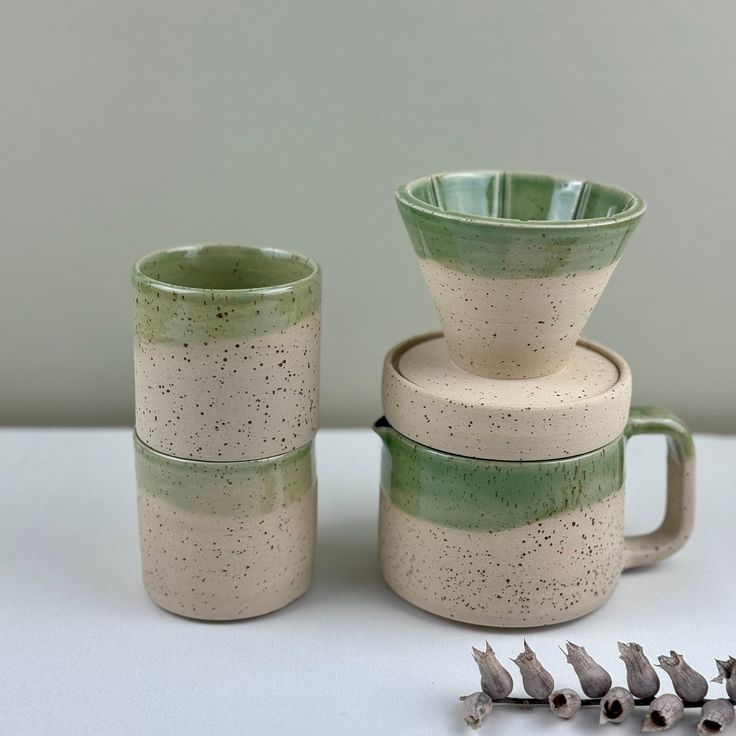 three ceramic cups sitting next to each other on a white tablecloth with tiny birds around them