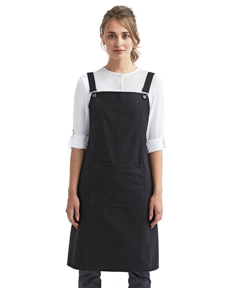 a woman standing wearing an apron and black pants with her hands in her pockets, looking at the camera