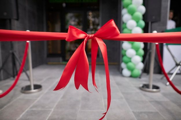 a red ribbon tied to a gate with green and white balloons in the back ground