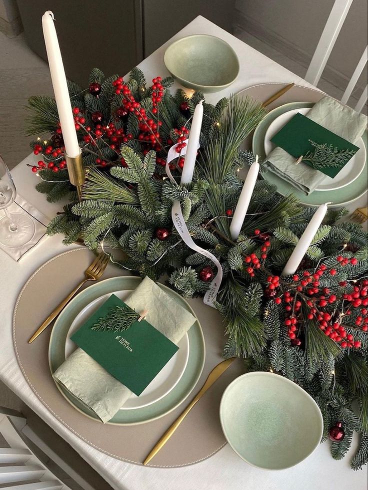 the table is set for christmas dinner with green napkins and red berries on it