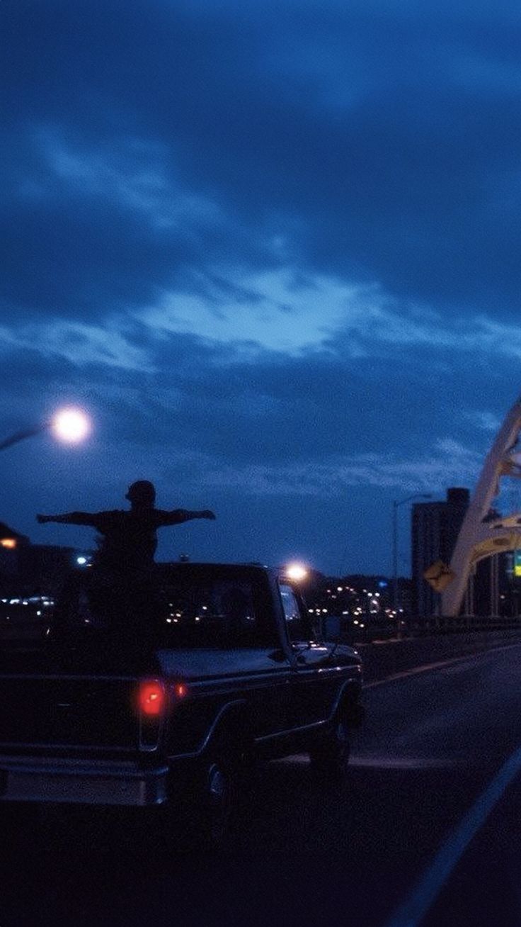 a man standing on the back of a truck in front of a bridge at night