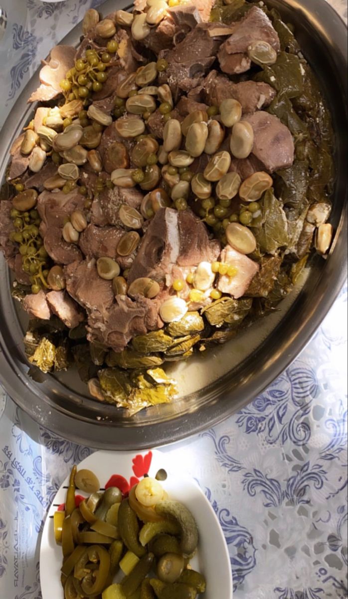 there is a platter with meat and vegetables next to a bowl of pickles