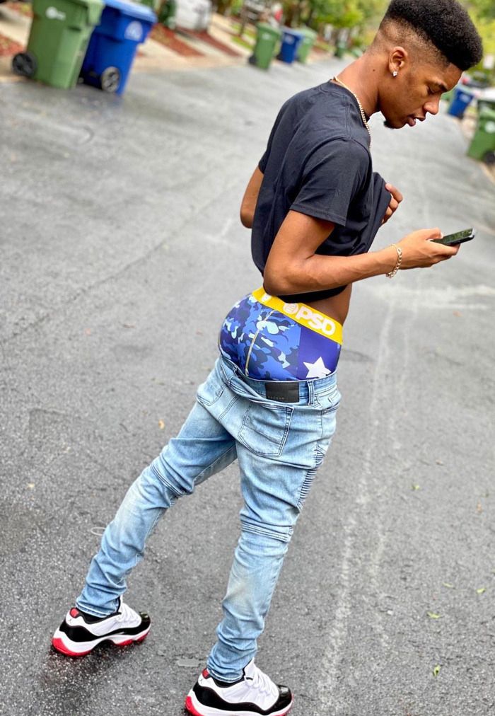 a young man standing in the street looking at his cell phone while wearing blue jeans