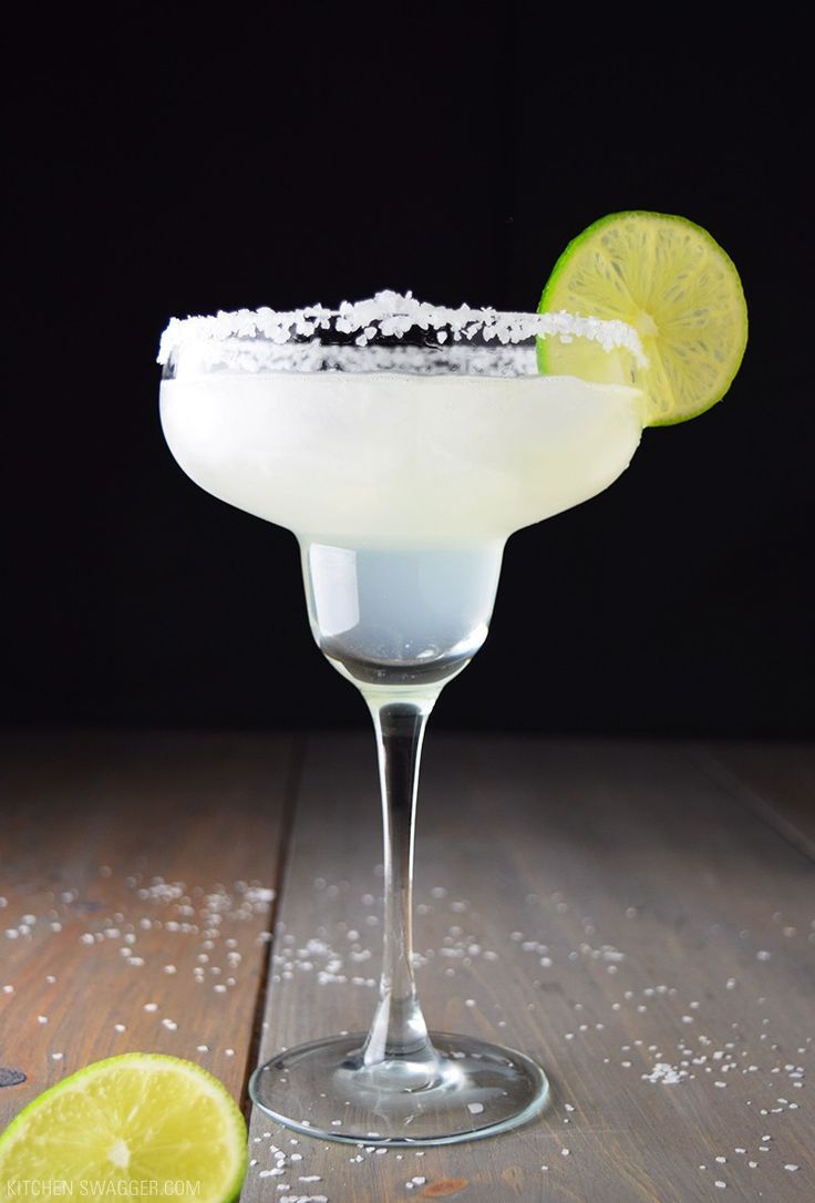 a margarita sitting on top of a wooden table next to a slice of lime and salt