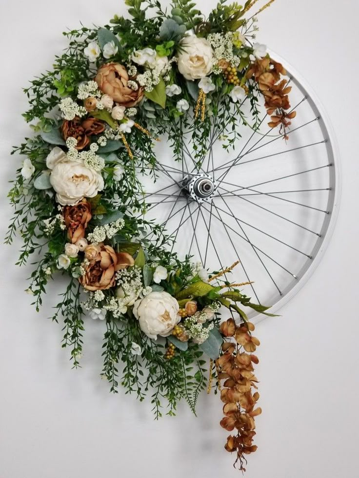 a bicycle wheel with flowers and greenery on the front is mounted on a wall