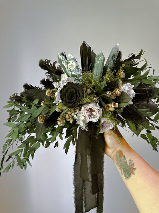 a hand holding a bouquet of flowers and greenery in front of a white wall