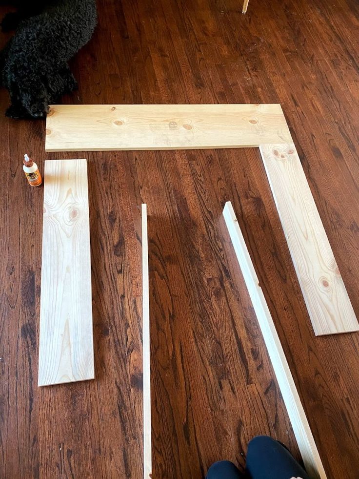 a black dog sitting on top of a wooden floor next to some pieces of wood