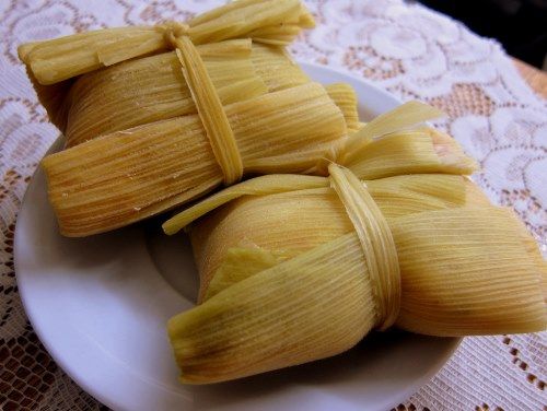 three tamales on a white plate sitting on a lace tablecloth