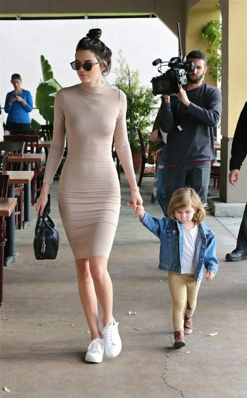 a woman walking down a sidewalk holding hands with a small child in front of her