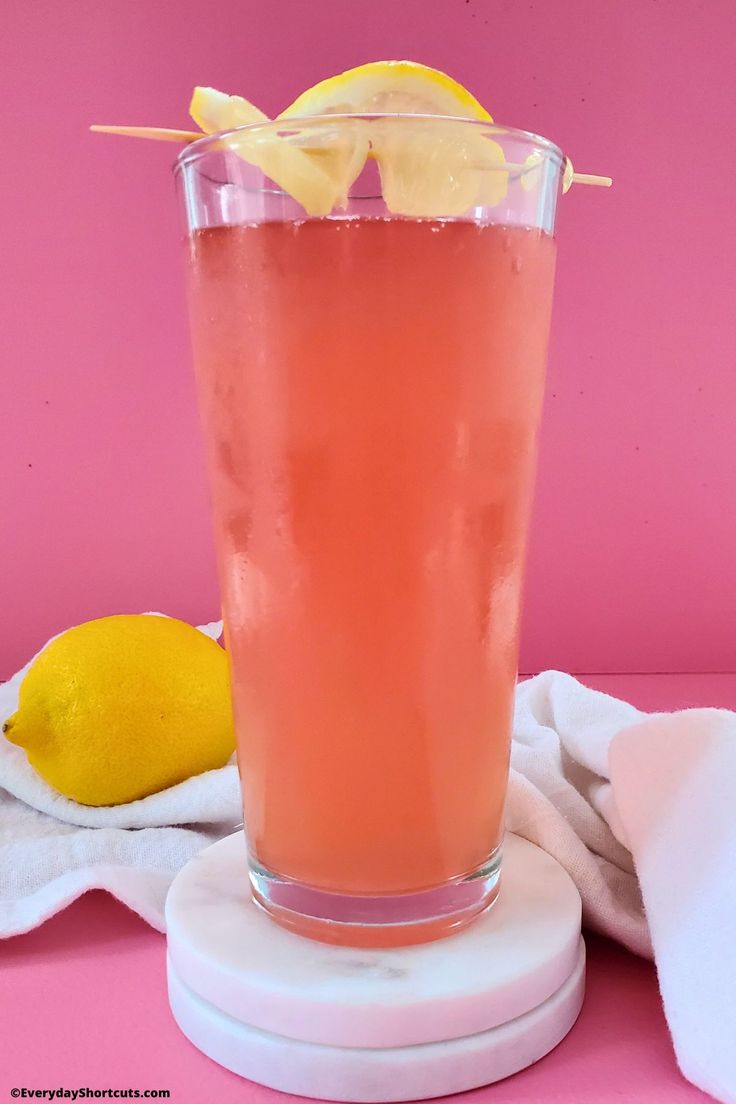 a pink drink in a glass with a lemon wedge on the rim and a towel next to it