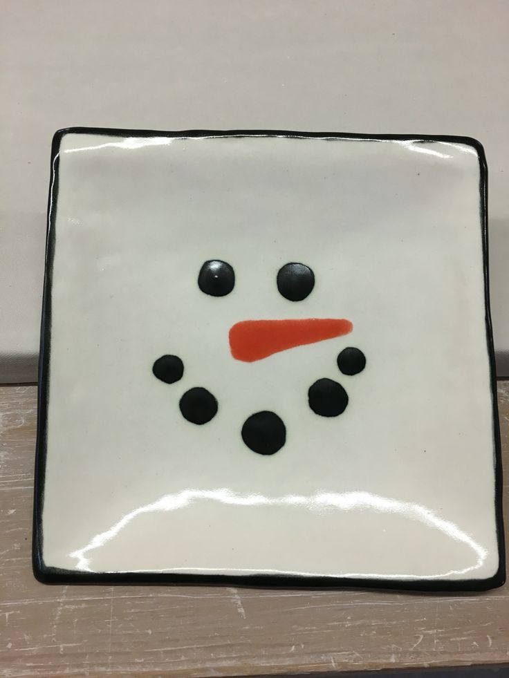 a white and black square plate with a snowman face on the front, sitting on a wooden table