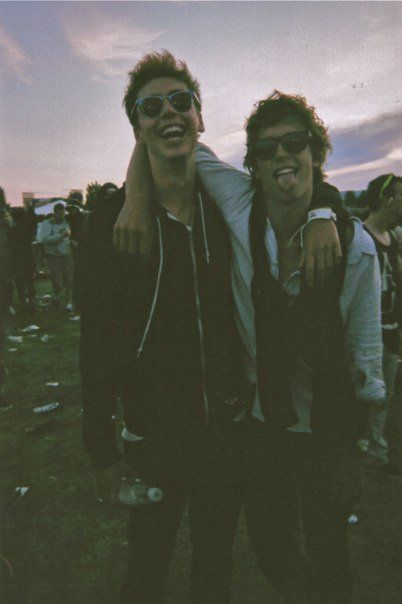 two young men standing next to each other on top of a grass covered field with people in the background