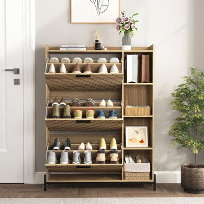 a wooden shoe rack filled with shoes next to a potted plant on top of a hard wood floor