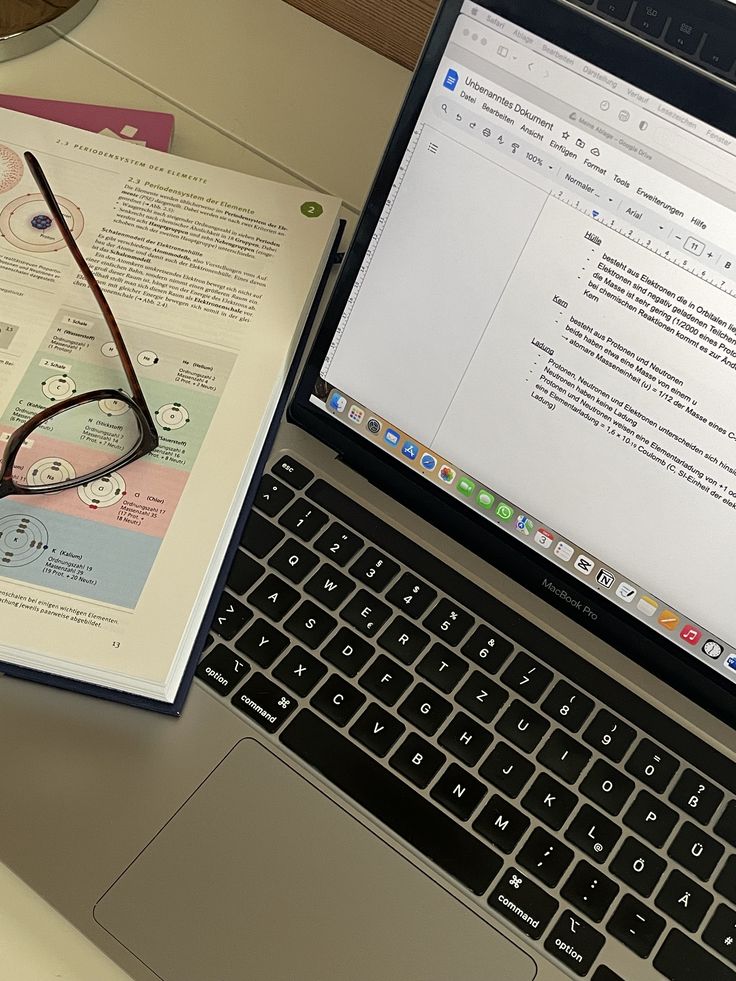 an open laptop computer sitting on top of a desk next to a book and glasses