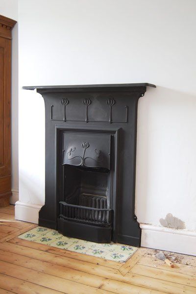 an empty room with a black fireplace and wooden floors in the corner, next to a white wall