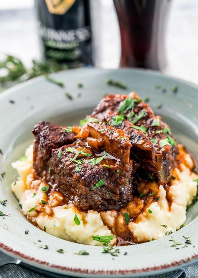 a white plate topped with meat and mashed potatoes next to a bottle of booze