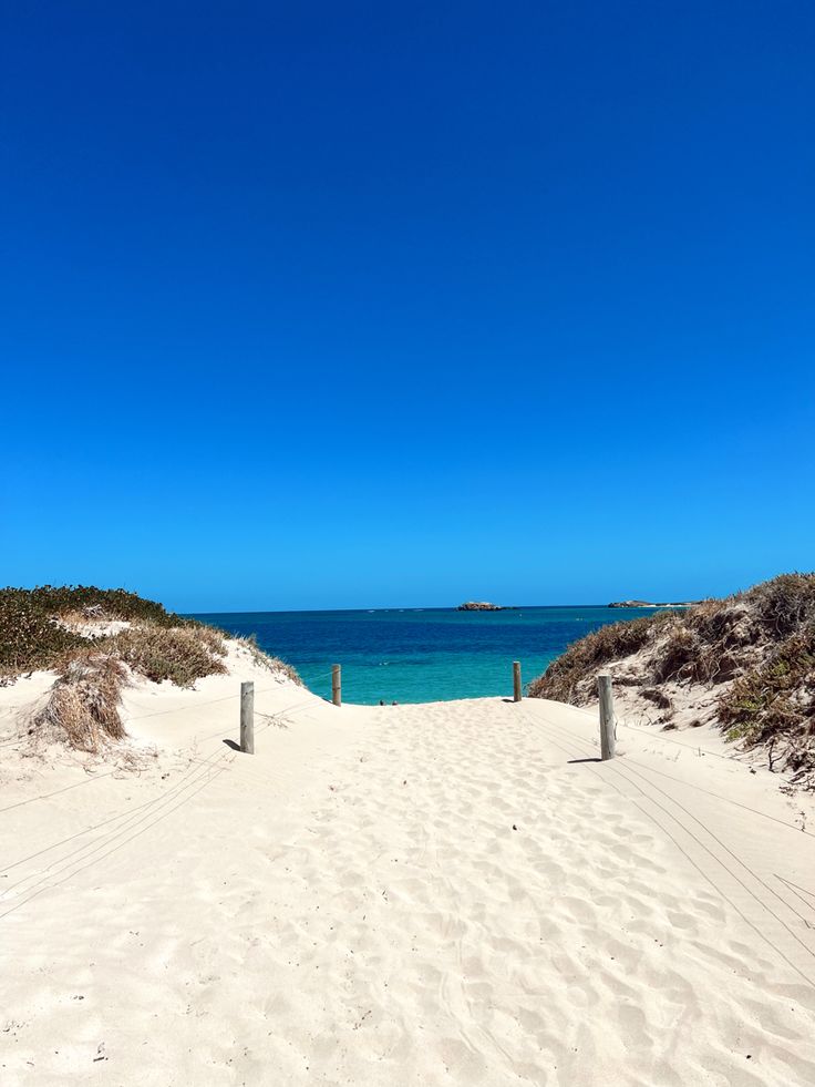 a sandy path leading to the ocean on a sunny day with clear blue skies in the background