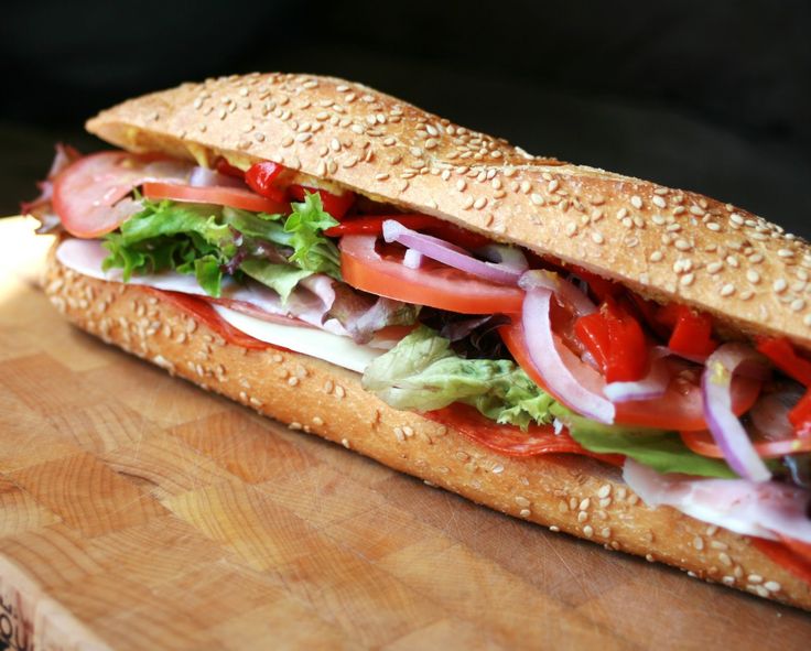 a sub sandwich with lettuce, tomato and onion on a wooden cutting board