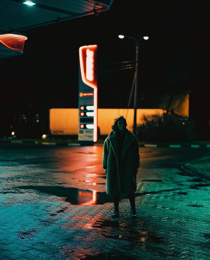 a person standing in the middle of an empty parking lot at night, wearing a long coat